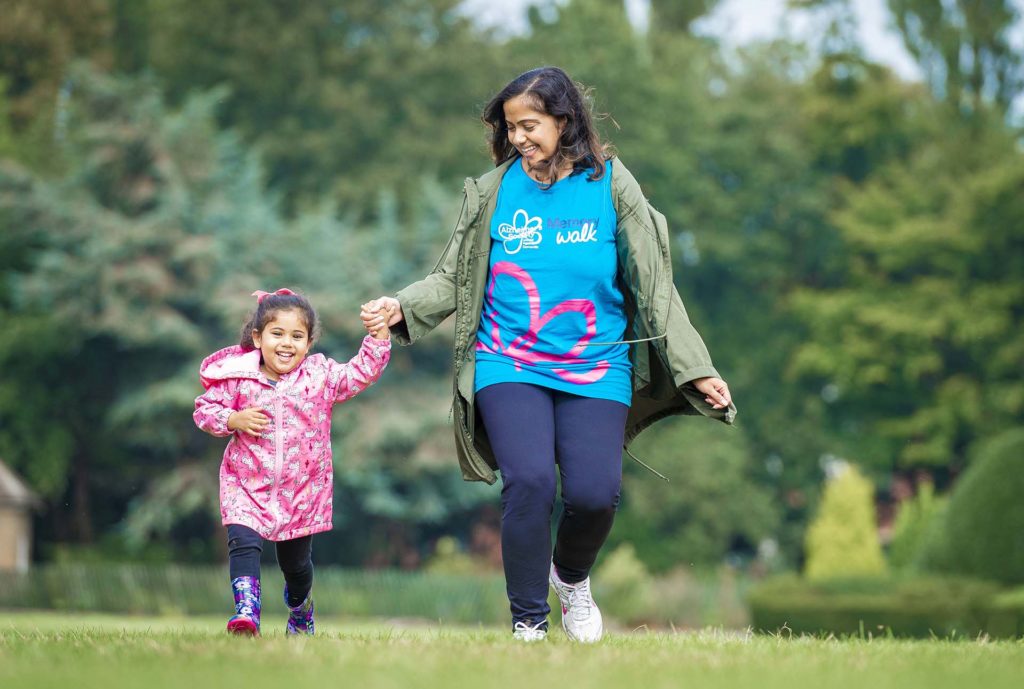 Mum, wearing Memory Walk T-shirt, and 5 year old daughter laughing as they walk in the park