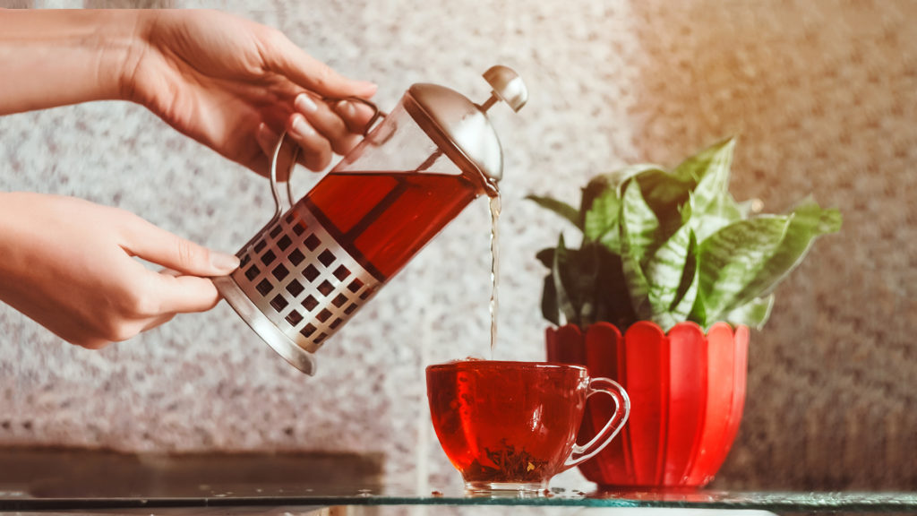 Woman's hands pouring red tea out of cafetiere