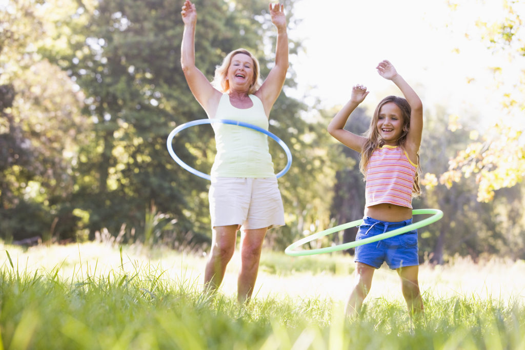 Grandmother and granddaughter at a park hula hooping and smiling; 