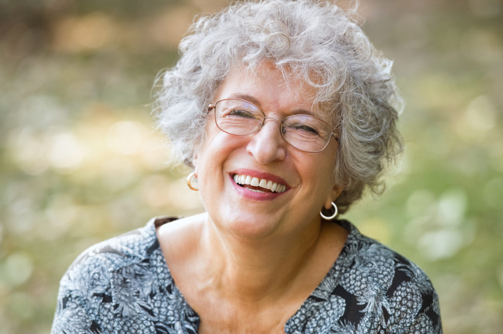 Portrait of senior woman smiling and looking at camera. Cheerful mature woman wearing eyeglasses in the park. Happy old woman with grey hair smiling. Carefree and positive retired woman.; 