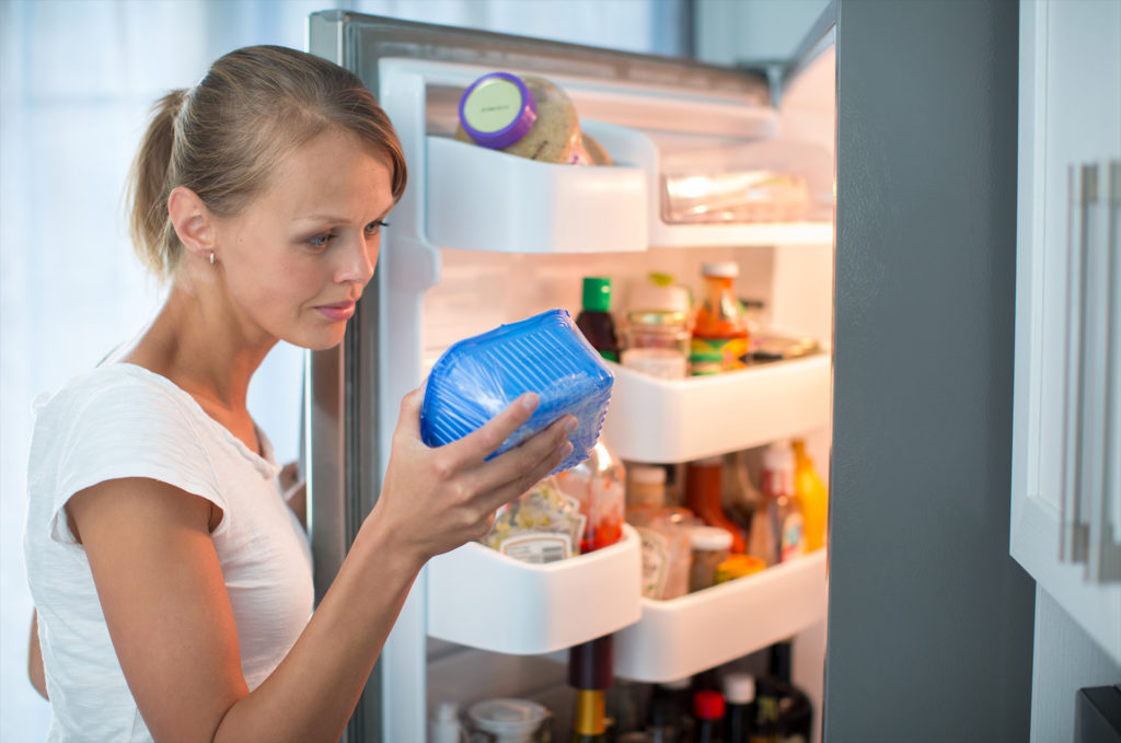 Is this still fine? Pretty, young woman in her kitchen by the fridge, looking at the expiry date of a product she took from her fridge