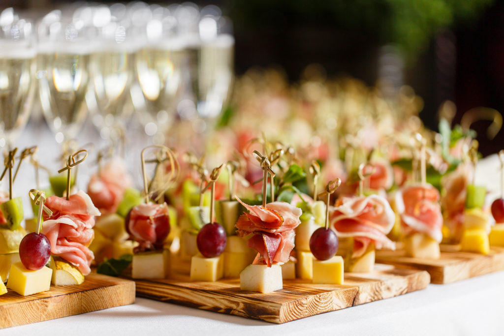 the buffet at the reception. Glasses of wine and champagne. Assortment of canapes on wooden board. Banquet service. catering food, snacks with cheese, jamon, prosciutto and fruit; 
