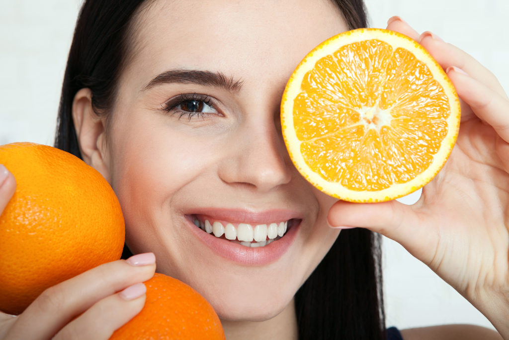 Woman holding up oranges cut in half to her face