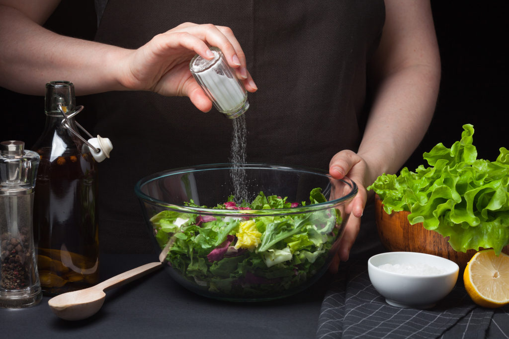 Woman chef in the kitchen preparing vegetable salad. Healthy Eating. Diet Concept. A Healthy Way Of Life. To Cook At Home. For Cooking. The girl sprinkles salt in a salad on a dark background; 