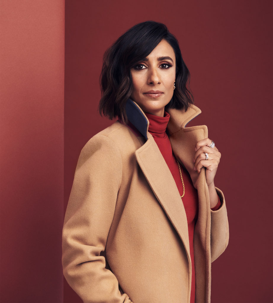 Young Asian woman in smart camel coat over red roll neck top, terracotta background