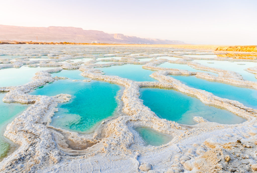 Series of turquoise pools with white salty edges, arid land beyond