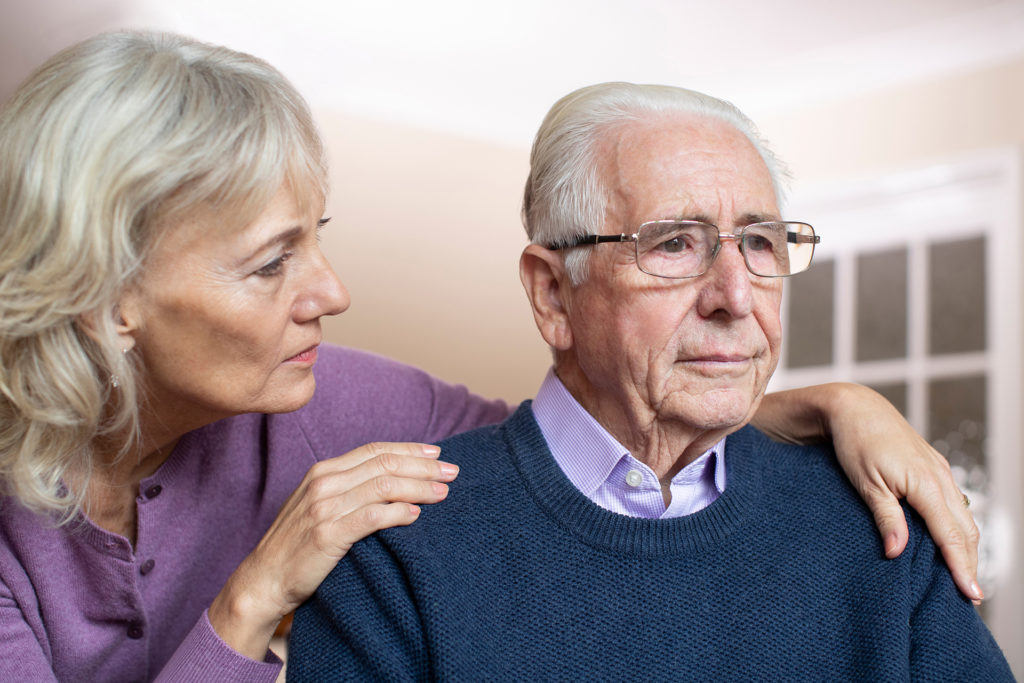 Confused Senior Man Suffering With Depression And Dementia Being Comforted By Wife; 