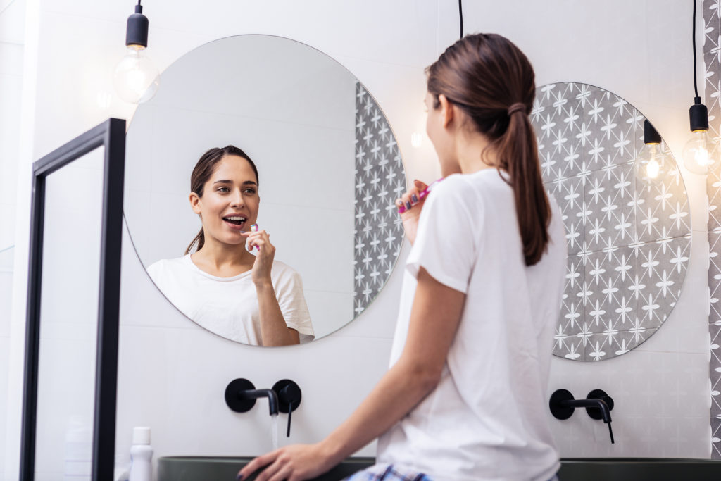 Circular mirror. Close up of appealing woman brushing teeth in front of circular mirror; 