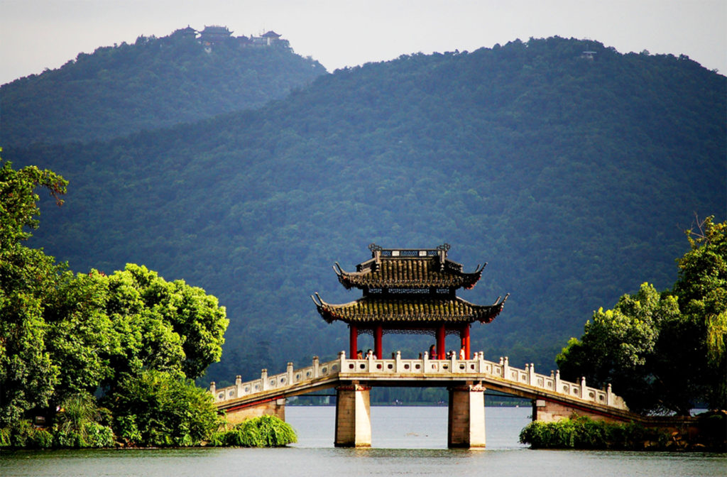 Chinese bridge and pagoda across lake, misty blue mountain beyond