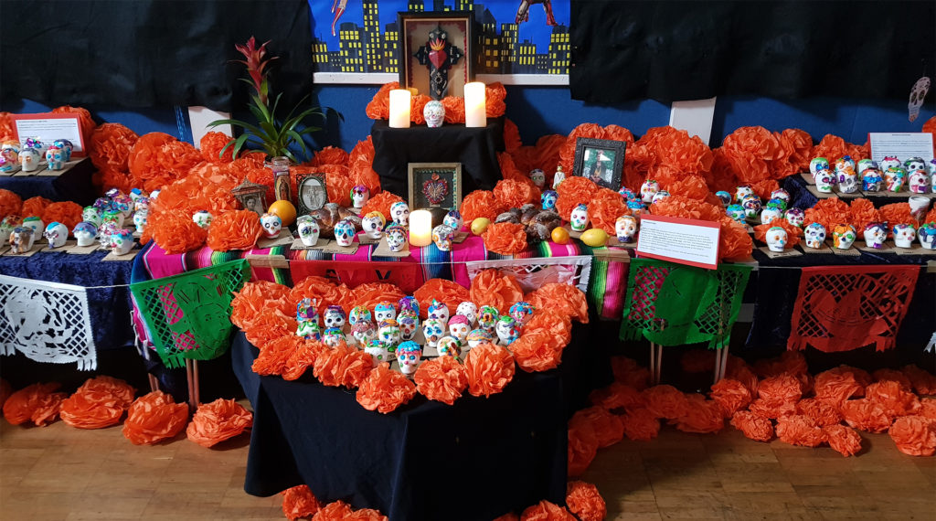 Table with orange paper flowers, sugar skulls, lemons, candles and photos of people