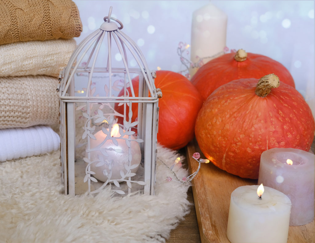 cozy Scandinavian hyugge, three orange pumpkins, white candles, woolen clothes, sheepskin, halloween concept, cozy home, aromatherapy