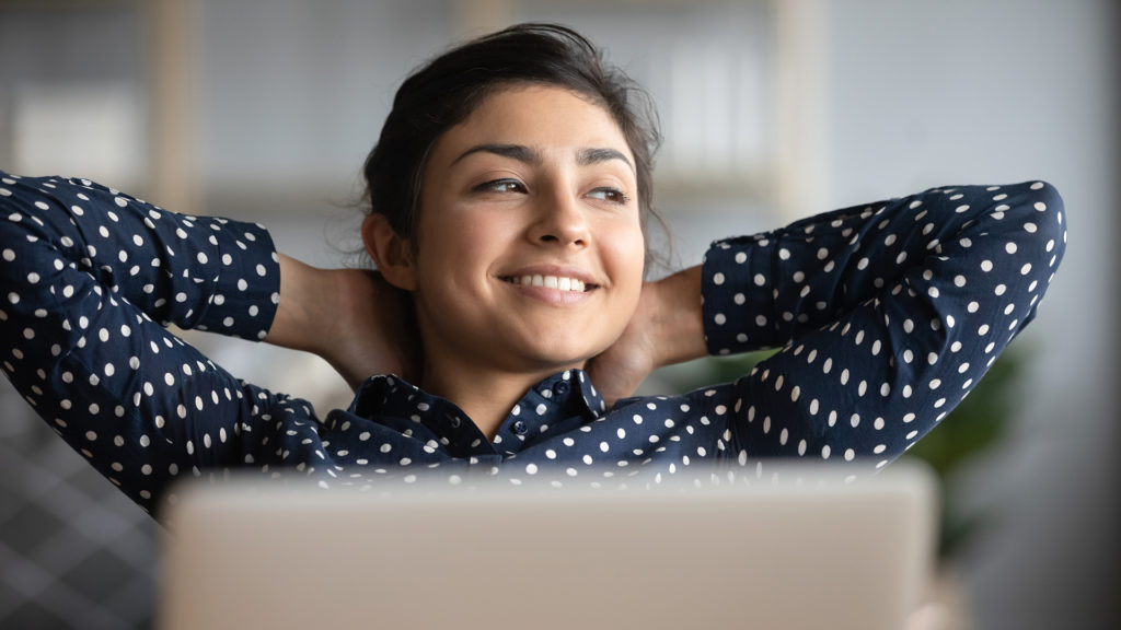 Happy satisfied indian woman rest at home office sit with laptop hold hands behind head, dreamy young lady relax finished work feel peace of mind 