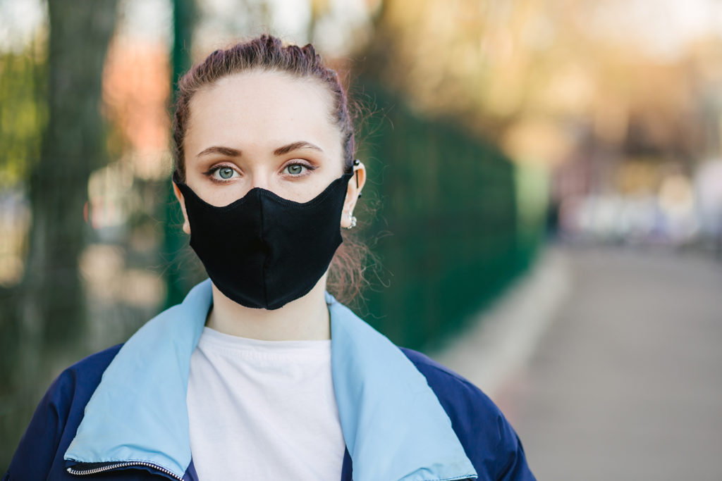 Closeup pretty woman wearing a face mask to protect against pollution or disease.COVID-19 Pandemic Coronavirus Young girl in city street wearing face protective mask.Copy space.Quarantine.Stay at home; 