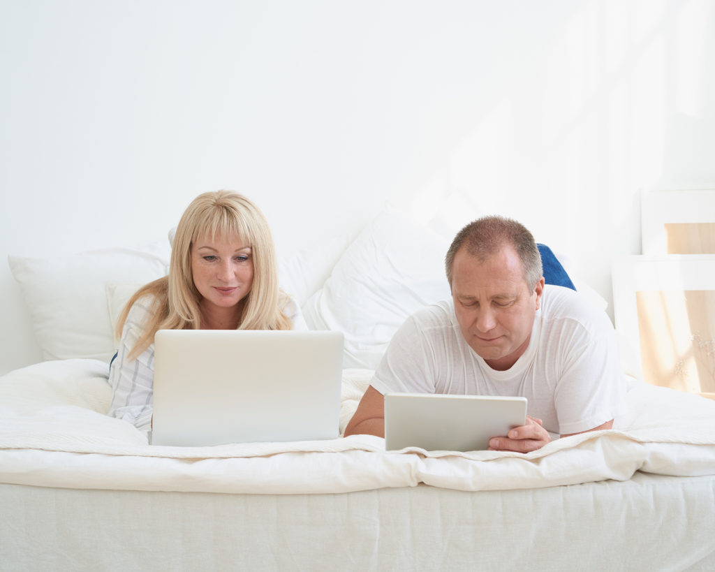 Mature married couple planning travel, choosing vacation, looking for tickets, booking hotel. Handsome man with tablet and attractive middle age woman with laptop spending time together