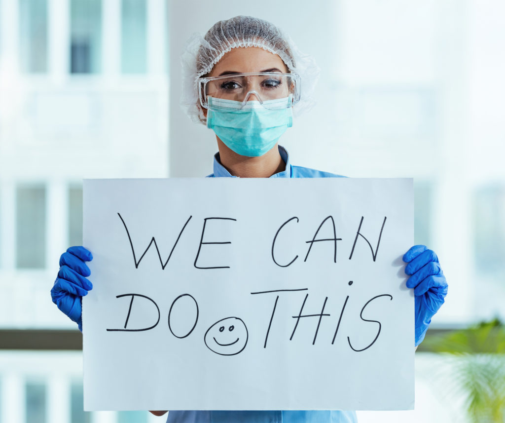 NHS nurse in mask and PPE holds up sign, We Can Do This