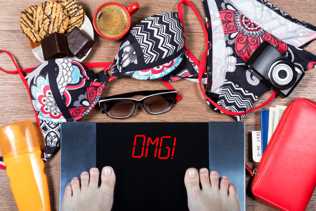 Woman weighs herself before vacation. Concept of unhealthy lifestyle and its consequenses. Digital scales with sign omg, holiday accessories and sweets. 