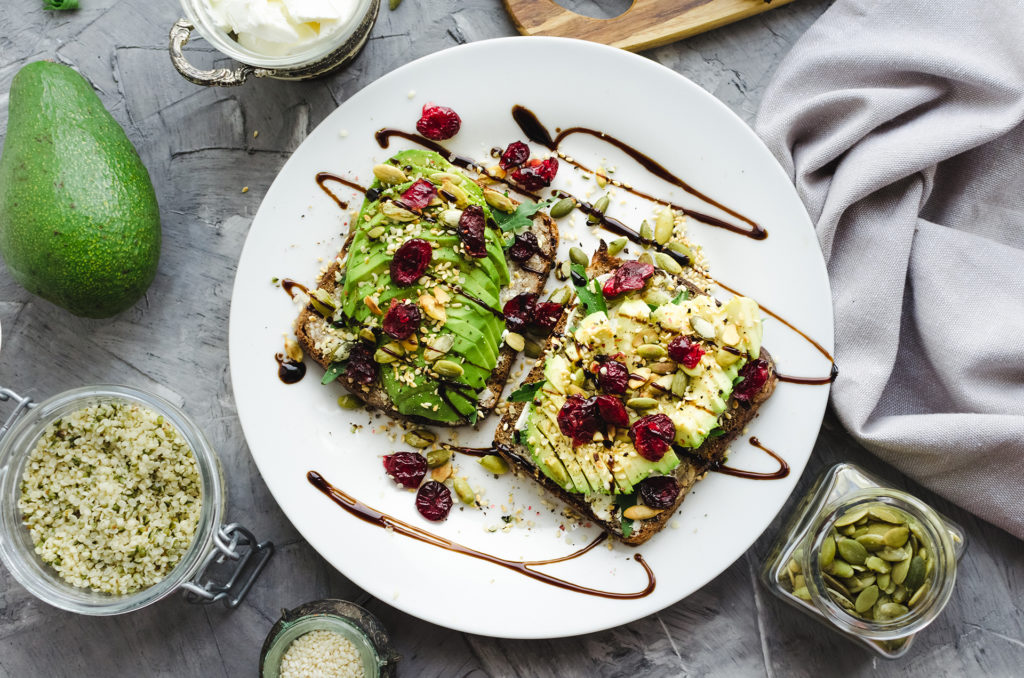 Healthy avocado toasts for breakfast or lunch with rye bread, cream cheese, arugula, sliced avocado, dried cranberry, pumpkin, hemp and sesame seeds. Vegetarian sandwiches. Clean eating