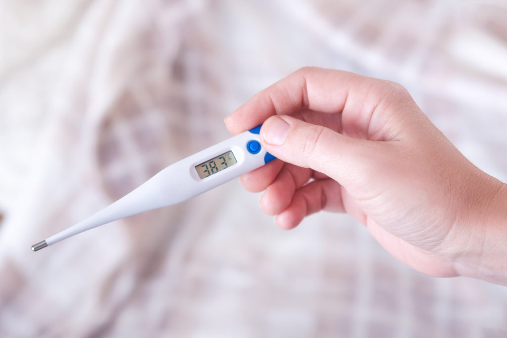Closeup shot of a woman looking at thermometer. Female hands holding a digital thermometer. Girl measures the temperature. Shallow depth of field with focus on thermometer.; 