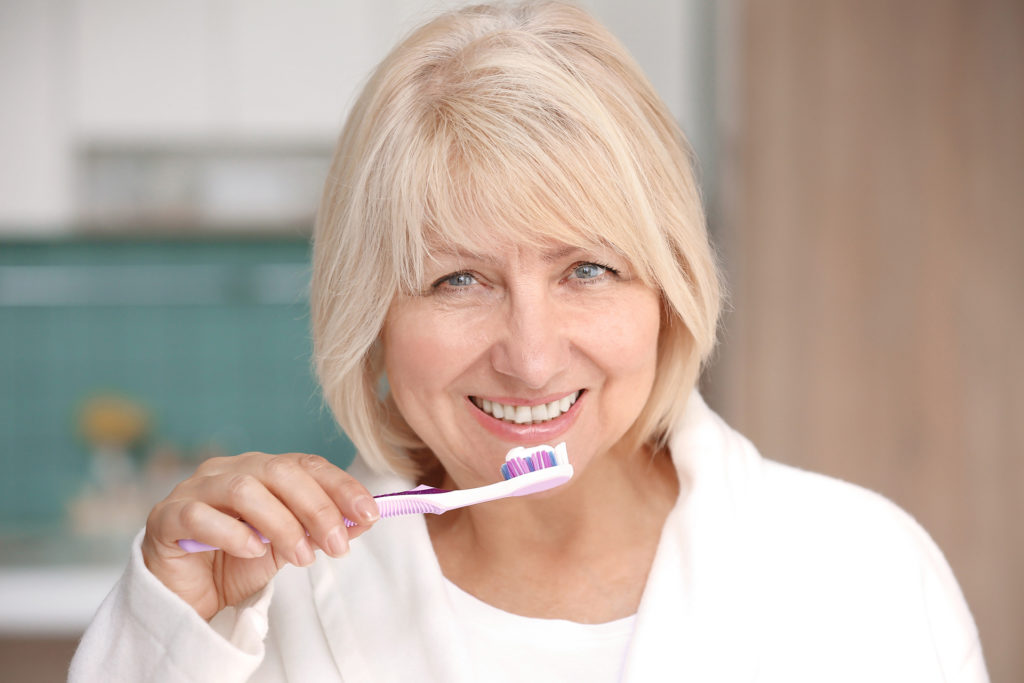 Mature woman cleaning teeth at home; 