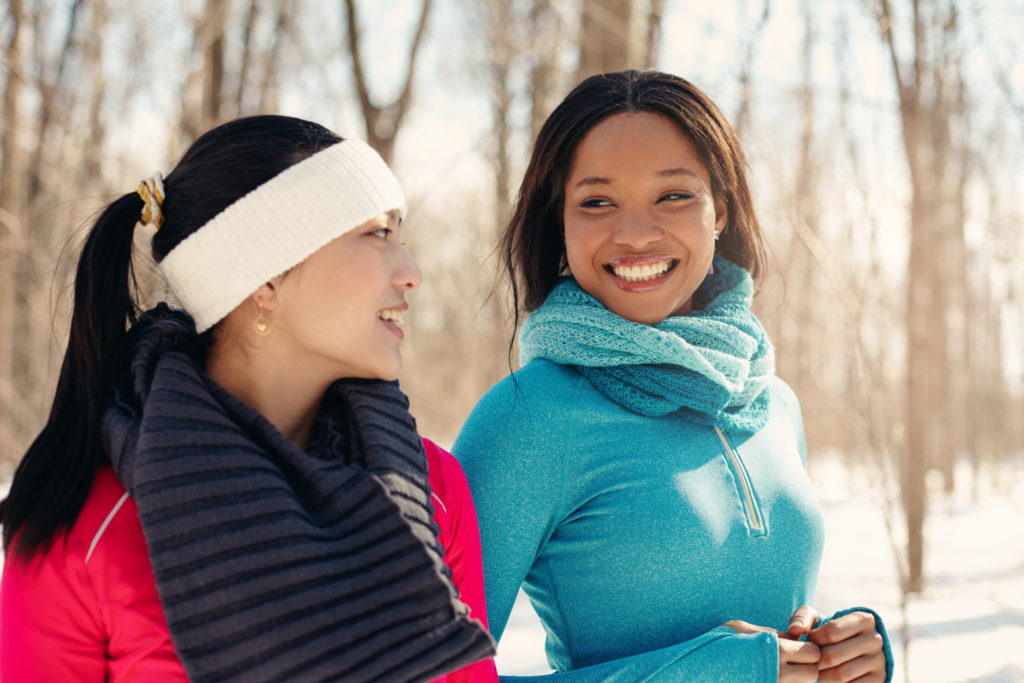 Multi-ethnic pair of female friends taking a break from jogging in the snow in winter; 
