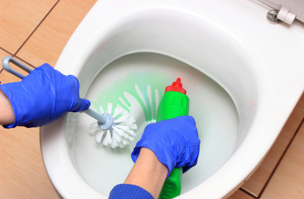 Hand of woman in blue glove cleaning toilet bowl using brush and detergent, concept for house cleaning and household duties; 