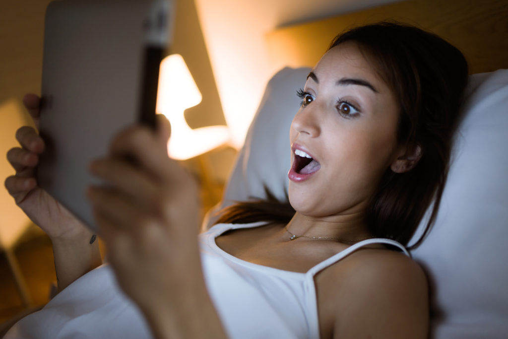 Portrait of surprised woman looking her digital tablet in the bed at night.; 