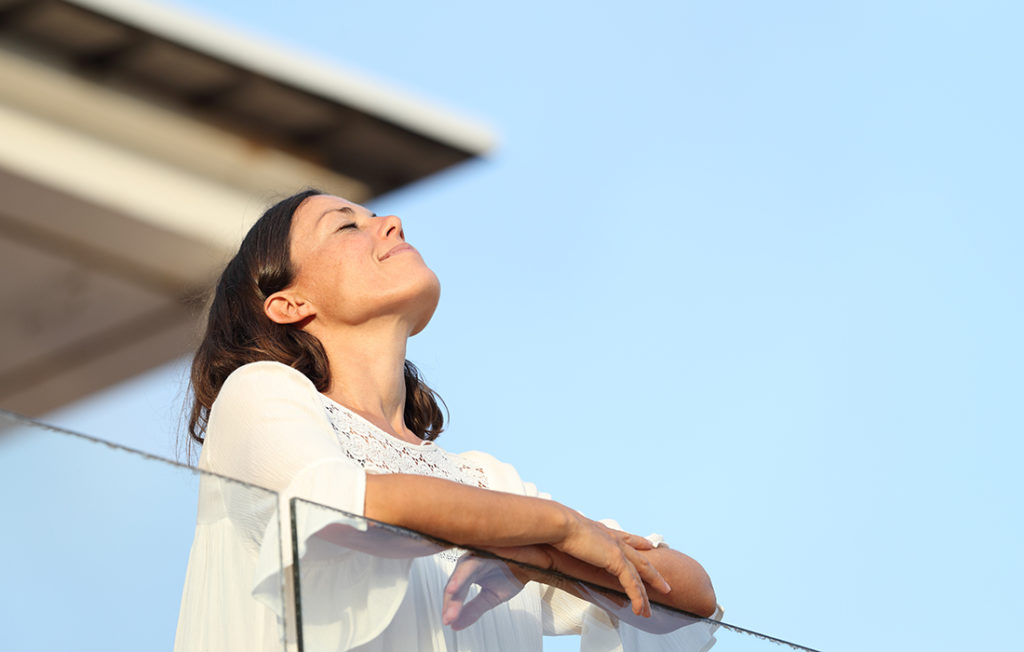 Relaxed adult woman breathing fresh air standing on a hotel balcony