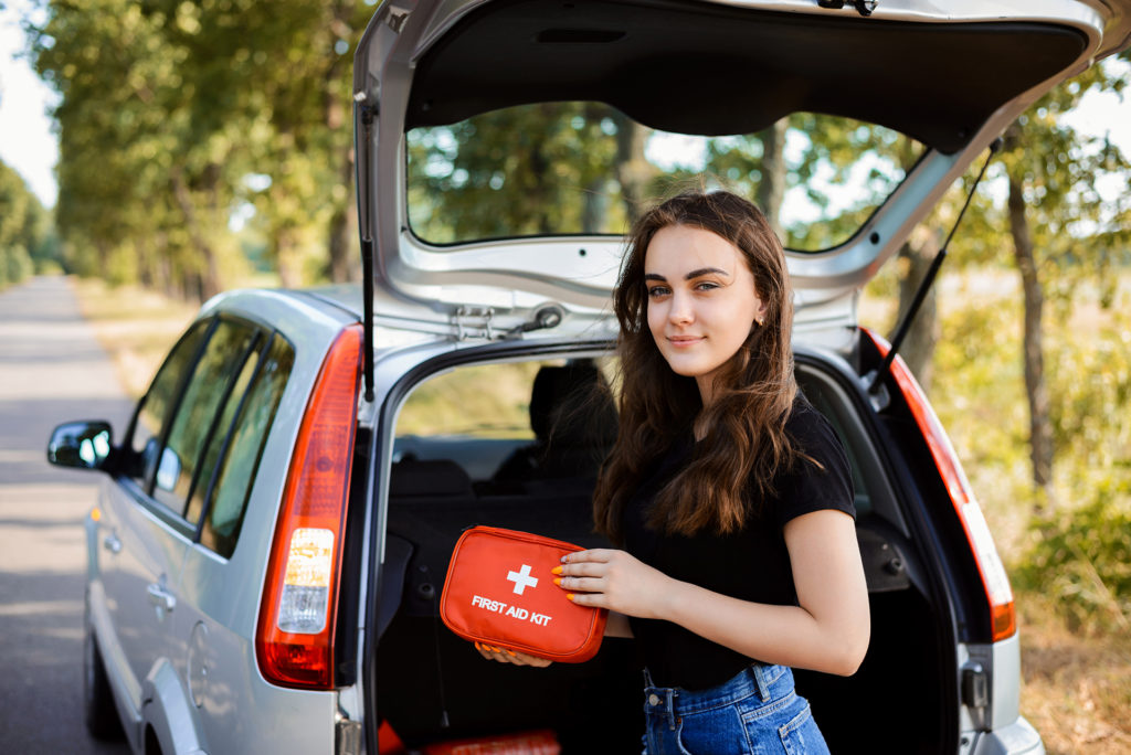 Young girl standing near open back door of silver hatchback car and shows first aid kit that must be in every car for emergency; Shutterstock ID 1464201608
