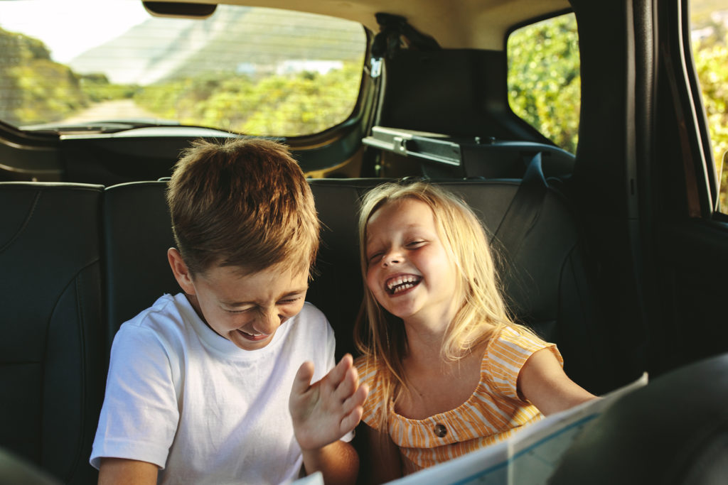 Siblings sitting on backseat of car looking at map and smiling. Kids traveling in a car on roadtrip playing with a map.; Shutterstock ID 1790116736