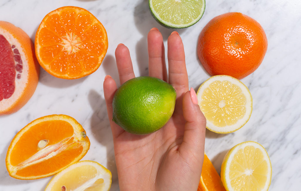 Citrus fruits. Orange, lemon, grapefruit, mandarin and lime on a trendy stone background. Top view, flat lay. Woman's hand grab or hold a piece; 