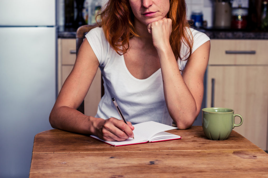 Woman sitting writing in notebook at kitchen table
