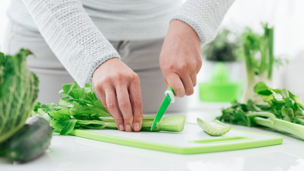 Woman's hands chopping celery on board in kitchen