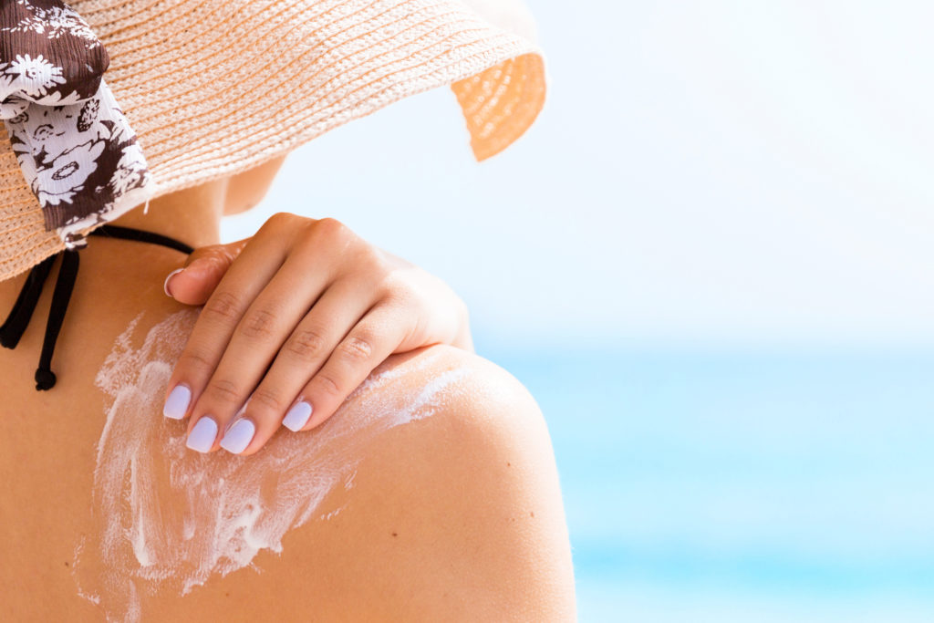 Woman wearing a hat put suncream on her shoulder