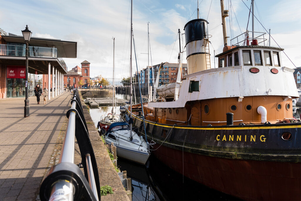 Tug boat moored at harbourside, brick building with tower in background