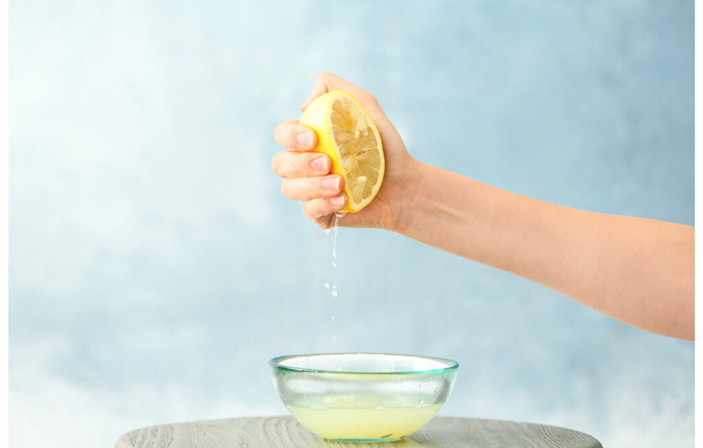 Young woman squeezing lemon juice into bowl on color background; 