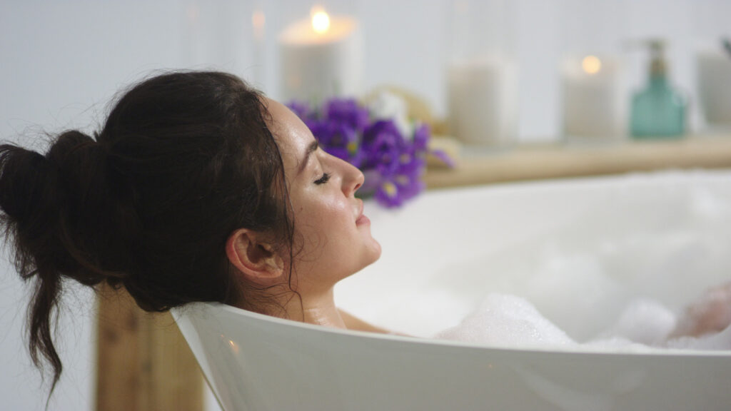 Brunette relaxing in foam bath with candles in background