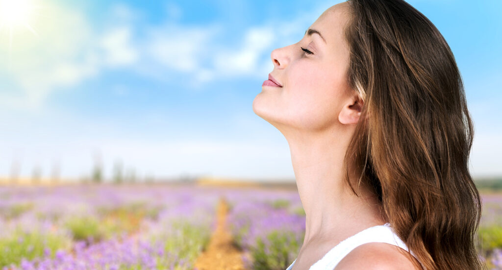 Woman taking deep breath with fields of flowers in background