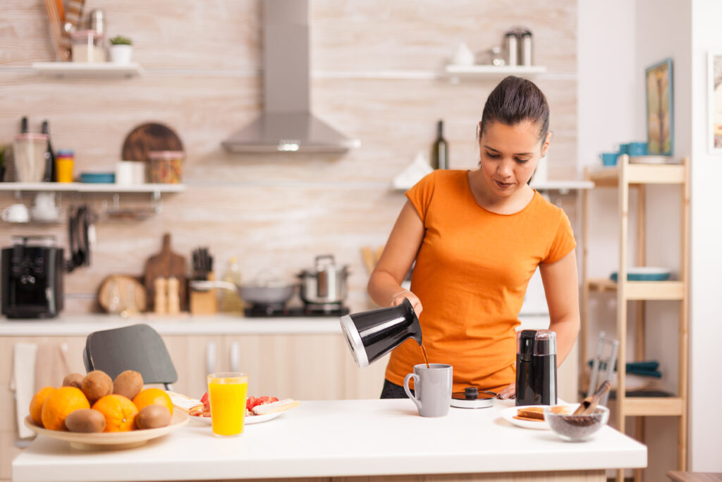 Woman pouring hot coffee in cup in the morning from pot. Housewife at home making fresh ground coffee in kitchen for breakfast, drinking, grinding coffee espresso before going to work; 