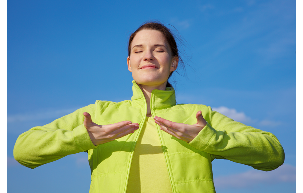 Brunette in lime green jacket doing breathing exercises outdoors